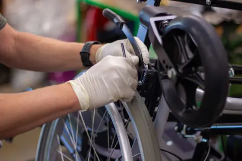 Mitarbeiter montiert mit Handschuhen ein Rollstuhlrad und befestigt es am Rollstuhl.