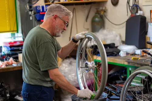Mitarbeiter reinigt einen Rollstuhlreifen in der Werkstatt mit einem Putztuch über einem Eimer.